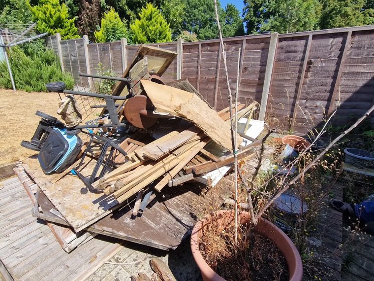 Pile of old decking, timber, garden furniture and junk on a patio before removal